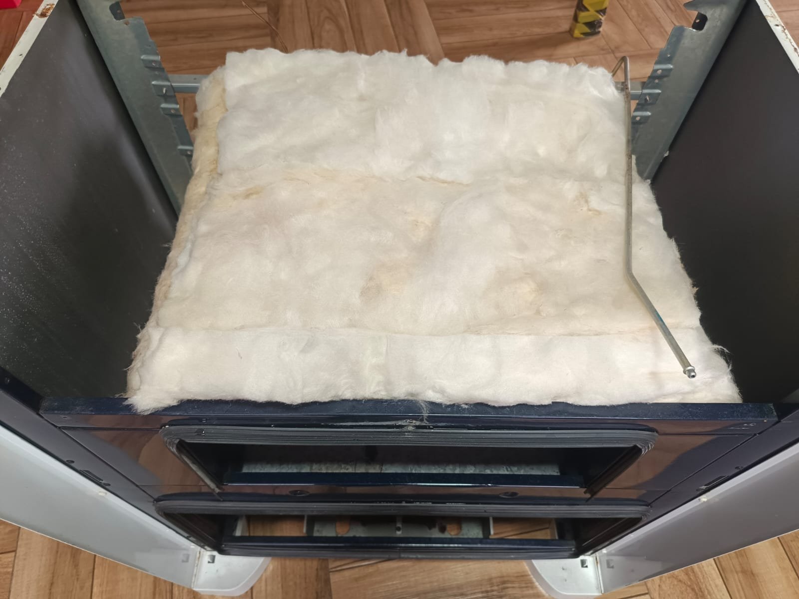 Foto de atendimento técnico com o isolamento interno de um forno exposto durante o serviço.